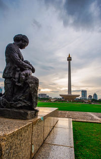 Statue in city against cloudy sky