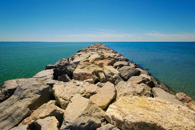 Rocks on sea shore against clear blue sky