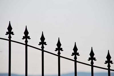 Low angle view of silhouette birds on railing against sky