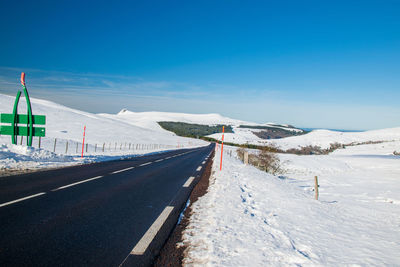 Road leading towards snowcapped mountain against blue sky