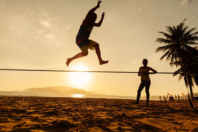 Man jumping at beach against sky during sunset