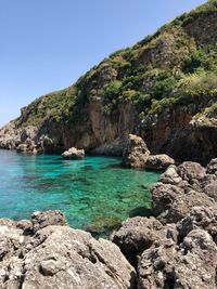 Scenic view of rocks by sea against clear sky