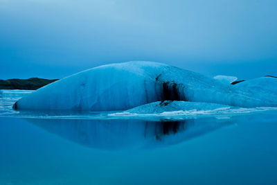 Iceberg on sea against blue sky at dusk