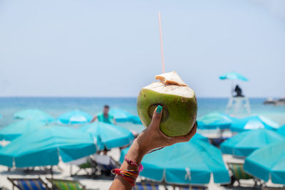 Close-up of man holding fruit on beach against sky