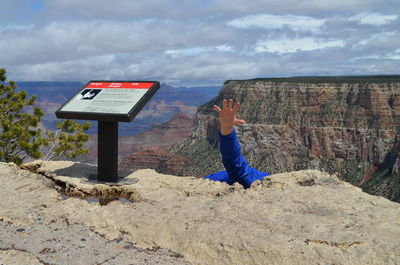 Cropped image of man reaching on top of mountain against sky