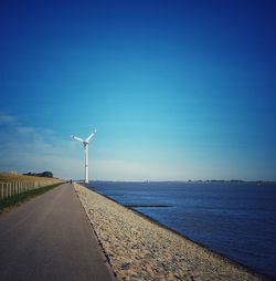 Wind turbines by road against clear blue sky