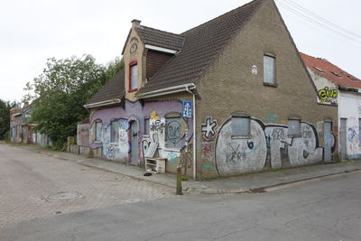 Graffiti on house by road against sky in city