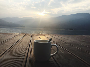 Coffee cup on table by mountains against sky