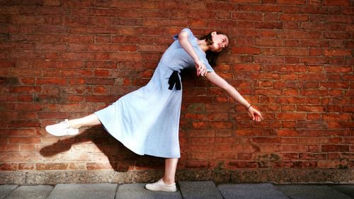 Rear view of smiling young woman against brick wall