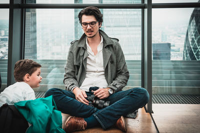 Young man using mobile phone while sitting on window