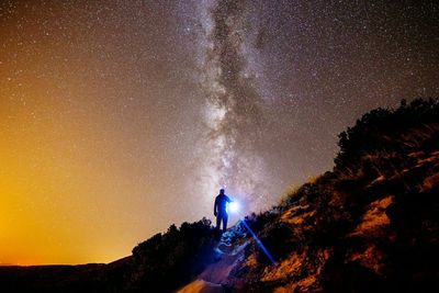 Low angle view of silhouette man with flashlight standing on mountain against star field at night