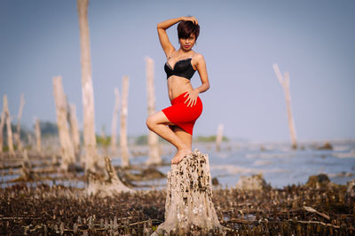 Woman standing on tree stump against sky