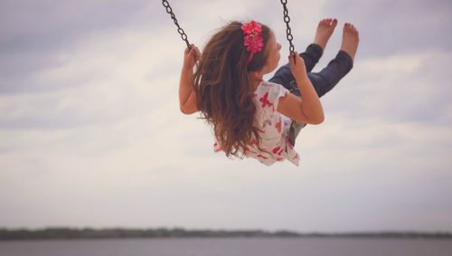 Full length of happy girl enjoying swing against sky