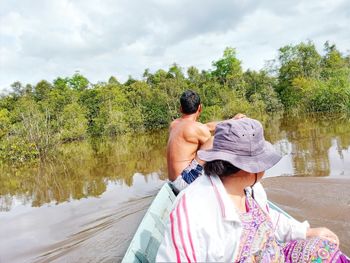 Rear view of people on lake against trees