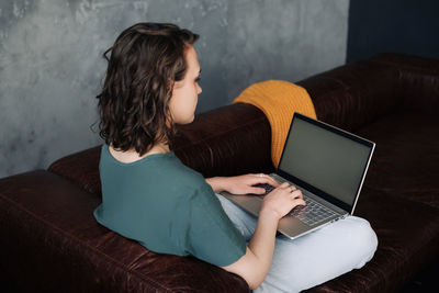 Woman using laptop while sitting on sofa at home