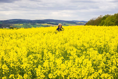 Woman standing amidst rape field against sky