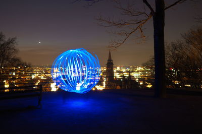 Illuminated ferris wheel against sky in city at night