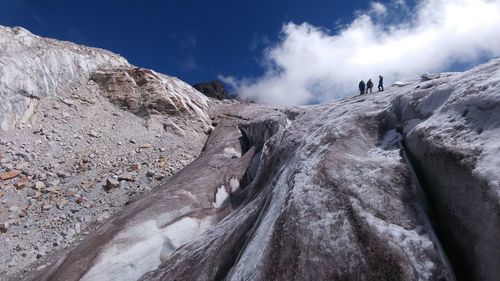 Low angle view of people on rock formation against sky