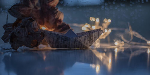 Close-up of paper boat by rock formation and illuminated lights on table