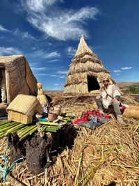 Woman wearing sunglasses sitting by hut against sky