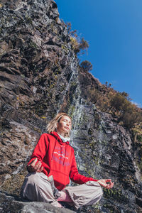 Low angle view of woman practicing yoga against waterfall on sunny day