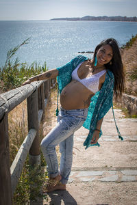Portrait of young pregnant woman standing against sea