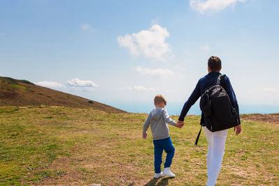 Rear view of father and son holding hands while walking on cliff