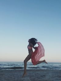 Woman with umbrella on beach against clear sky