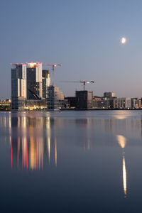 Illuminated city by river against sky