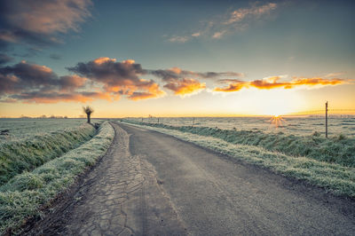 Road amidst field against sky during sunset