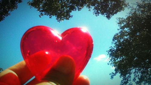 Close-up of hand holding heart shape against blue sky