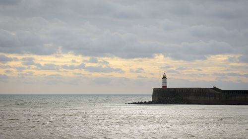 Lighthouse in sea against cloudy sky