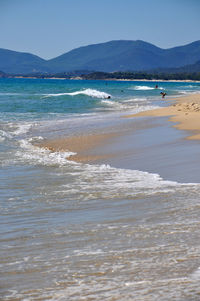 Scenic view of sea by mountains against clear sky