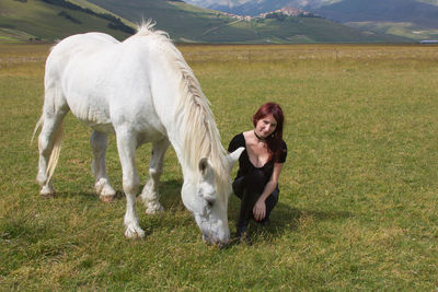 Portrait of smiling woman crouching by horse grazing on field