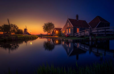 Scenic view of lake by buildings against sky during sunset