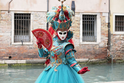 Woman in carnival costume standing by canal in city