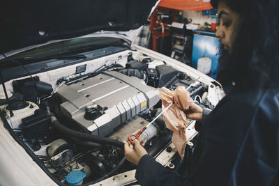 Female mechanic cleaning dipstick with paper at auto repair shop