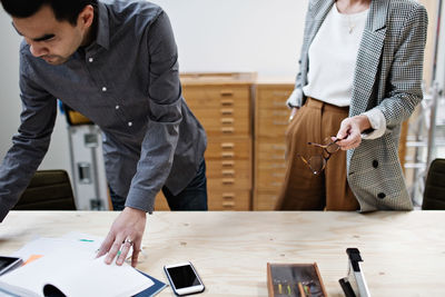 Serious businessman reading file while standing with female colleague at table in office