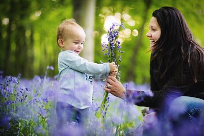 Mother giving flowers to cute son while crouching on field in park