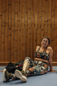 Smiling female athlete relaxing while sitting on floor at sports court