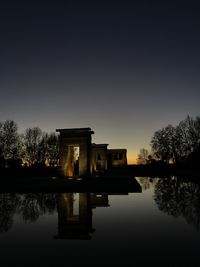 Silhouette building by lake against clear sky