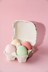 Close-up of multi colored eggs in carton on pink background