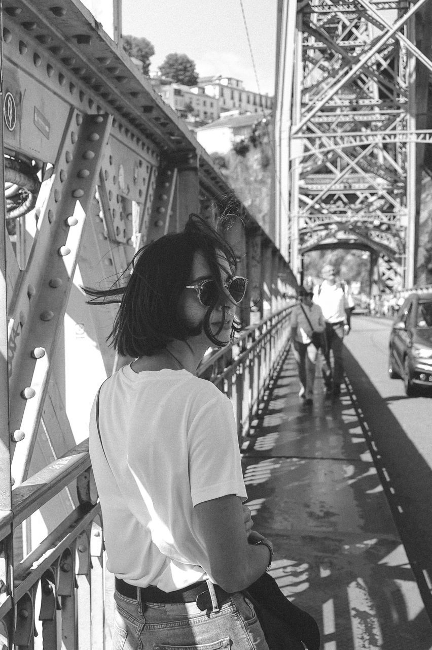 real people, one person, architecture, lifestyles, leisure activity, built structure, transportation, casual clothing, day, connection, bridge, women, side view, standing, focus on foreground, railing, young adult, city, bridge - man made structure, outdoors, hairstyle