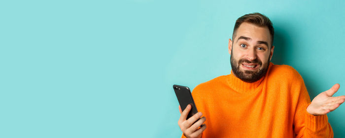 Portrait of young man using mobile phone against blue background