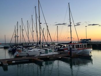 Sailboats moored in harbor at sunset