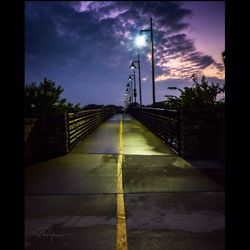 Road leading towards city against sky at sunset