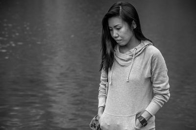 Beautiful woman with hands in pocket standing by lake