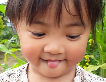 Close-up of cute girl sticking out tongue against plants