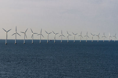Wind turbines by sea against sky