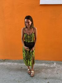 Portrait of smiling woman standing against orange wall